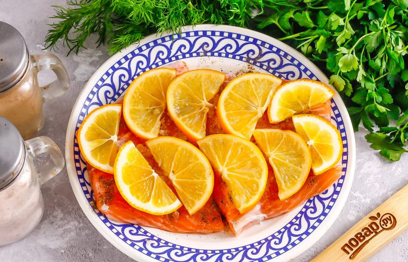 1. Этап. Засолка красной рыбы с лимоном: Лимон ошпарьте кипятком и нарежьте его половину ломтиками, удаляя косточки. Выложите на рыбу.
