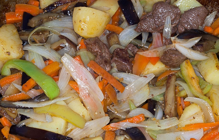 1. Этап. Баклажаны в казане на костре: Добавьте все овощи обратно в казан к баранине. Жарьте блюдо до готовности, помешивая.