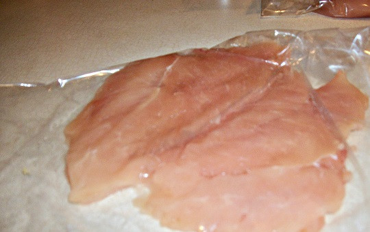 1. Этап. Фаршированная куриная грудка: 2. На рабочий стол положить пищевую пленку и кусочек филе. Накрыть еще одним слоем пленки и аккуратно отбить. Тут важно не применять силу, чтобы фаршированная куриная грудка в домашних условиях не была с дырками, но разбить уплотнения, сделав слой филе одинаковой толщины по всему периметру.