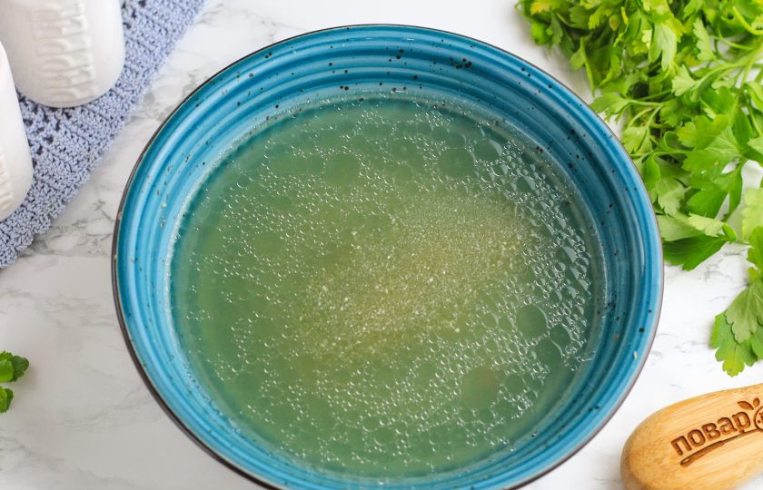 1. Этап. Заливное Провансаль из говядины: Процедите бульон через ситечко с мелкими ячейками или двойной слой марли. Разлейте на две пиалы: в одну чуть больше, а в другую — чуть меньше бульона. Всыпьте половину желатина в ту пиалу, где больше бульона и перемешайте. Дайте набухнуть 5 минут и снова перемешайте.