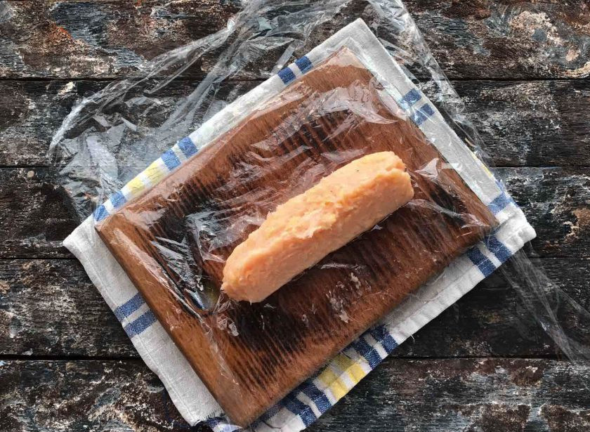 1. Этап. Домашние сосиски с сыром: Разложите пищевую пленку на разделочную доску, выложите куриный фарш, сверните, отрежьте пленку ножом по разделочной доске и скрутите края.