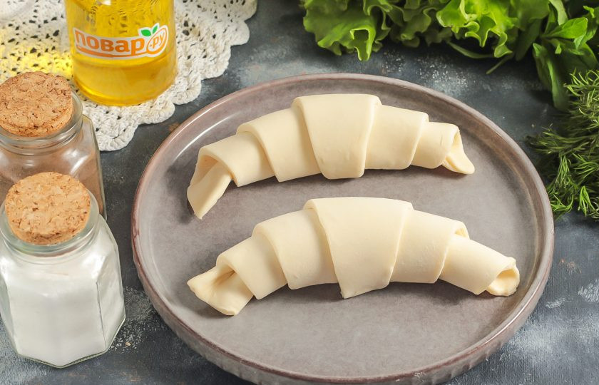 1. Этап. Круассаны с куриным салатом внутри: Слоеное тесто разморозьте, нарежьте длинными треугольниками и скатайте каждый из них рулетиком, начиная от края с двумя углами и заканчивая одним углом посередине.