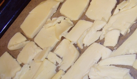 1. Этап. Сырный рулет с лососем: Разогреваем духовку до 200 градусов. Нарезаем твердый сыр не очень тонкими ломтиками, выкладываем его слоем (прямоугольной формы) на пергамент.