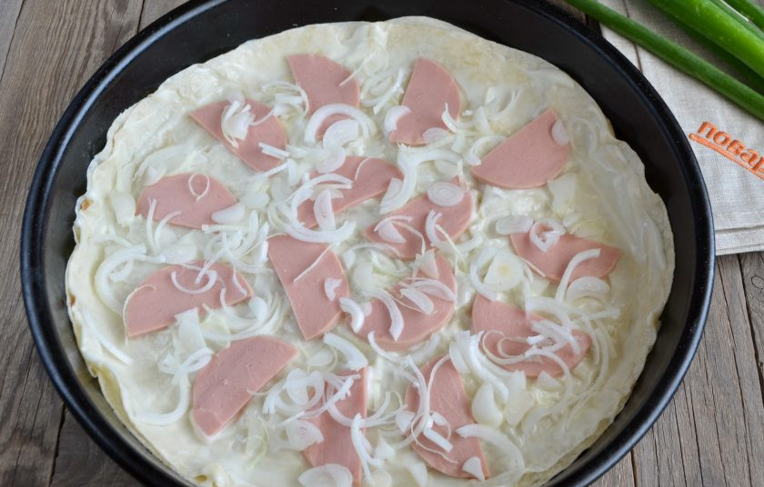 1. Этап. Пицца на лаваше в духовке: Порежьте полукольцами лук и колбаску. Распределите равномерно.