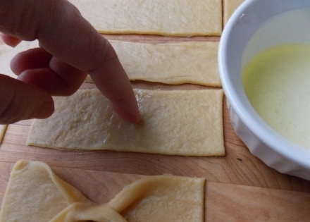 1. Этап. Печенье Бантики: Полоски под бантики получаются 3 на 6 см. Возьмите белок, отставленный ранее, и смажьте центр, потом заверните края внутрь, сформировав бантик.