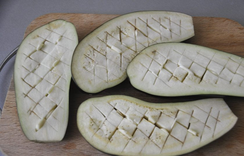 1. Этап. Греческая закуска Мелидзана: Баклажаны промойте и обсушите, нарежьте вдоль пополам, сделайте надрезы на мякоти баклажана, не прорезая насквозь. Порежьте 2 зубчика чеснока на пластинки и вставьте их в прорези.