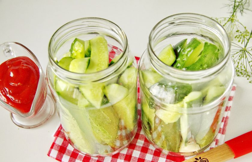 1. Этап. Огурцы с кетчупом на зиму: Предварительно простерилизуйте банки любым удобным способом и выложите на дно очищенные зубчики чеснока, перец горошком, лист хрена, лаврушку и зонтики укропа (всю зелень необходимо помыть). Плотно уложите огурцы в банки, чем плотнее получится, тем - лучше.