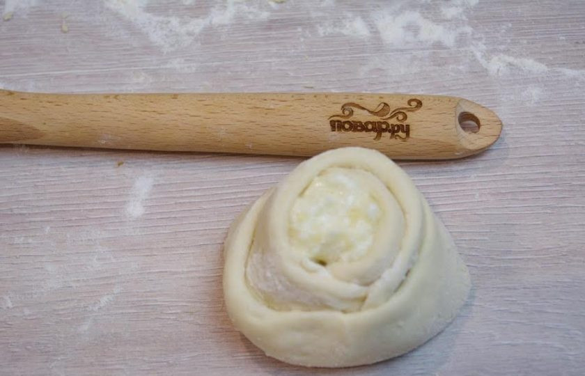 1. Этап. Ватрушки с творогом: 6. Приподнимите один сектор блинчика за два кончика. Оберните эту часть теста вокруг творога и закрепите, склеив края. Теперь возьмите вторую часто сектора. Оберните вокруг начинки и первого сектора. Так же поступите с последней частью сектора.Хорошо закрепите края. Получилась розочка.