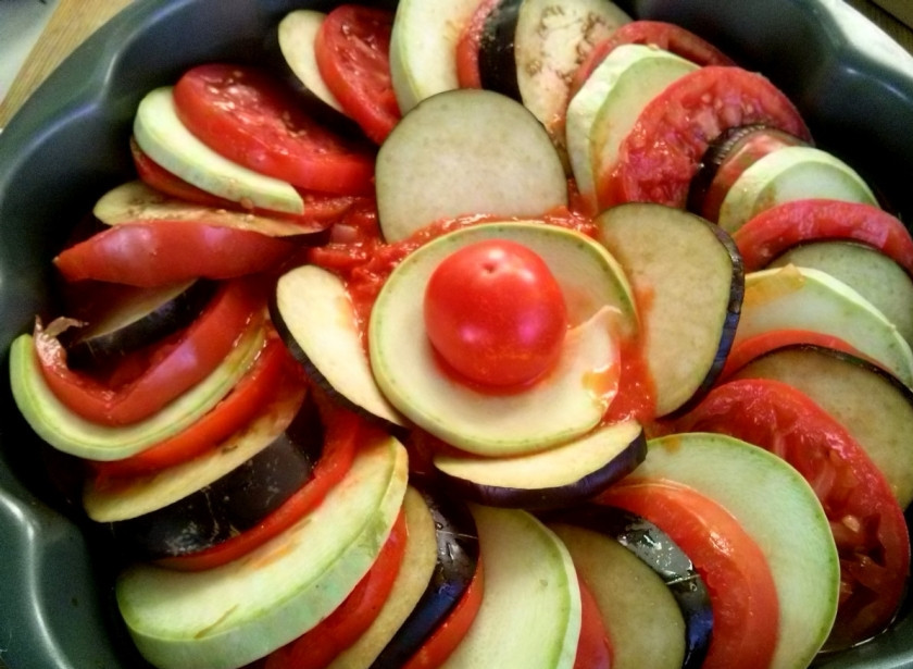 1. Этап. Рататуй из баклажанов и кабачков: 6. Готовый соус вылейте в жаропрочную форму. Затем уложите в получившийся соус кружки баклажанов, кабачков и помидоров, чередуя их один за другим. Сверху полейте 2 столовыми ложками соуса. Запекайте в духовке в течение 55 минут при 180 градусах. Перед употреблением дайте блюду остыть и настояться.