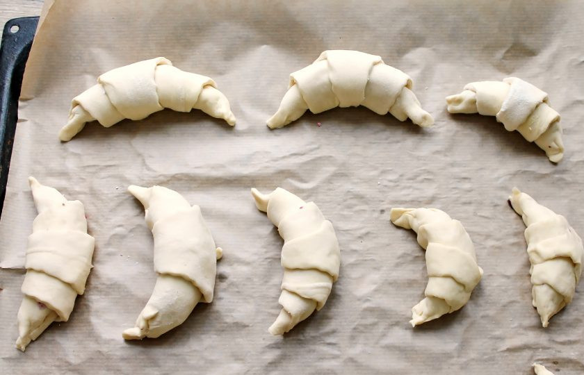 1. Этап. Круассаны с черникой: Сверните круассаны, начиная с широкой стороны, защипайте края. Придав форму полумесяца, выложите на противень с пергаментом.