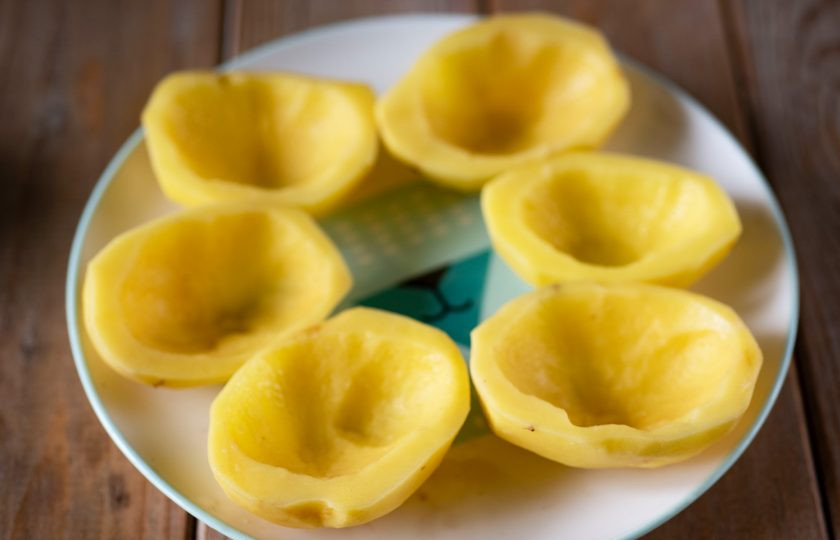 1. Этап. Картофель, фаршированный с рисом: Крупный картофель помойте, почистите и еще раз помойте. Очищенные клубни разрежьте каждый на 2 части. В каждой картофельной половинке ложечкой вырежьте выемки, как на фото.