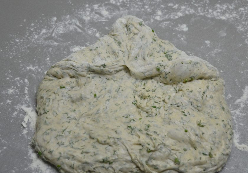 1. Этап. Хлеб с укропом: Присыпьте рабочую поверхность стола мукой, выложите тесто, растяните его в прямоугольник. Подверните уголки прямоугольника внутрь.