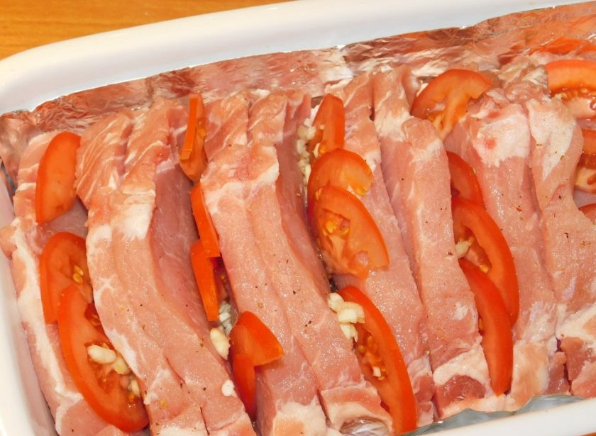 1. Этап. Фаршированная свинина из духовки: Начините помидорами и чесноком каждую вторую прорезь.