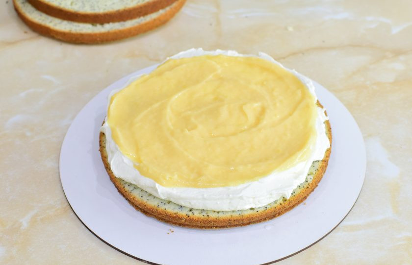 1. Этап. Лимонно-маковый торт: Коржи можно пропитать сахарным сиропом или водой. Выложите первый слой бисквита и распределите по нему крем, формируя по бокам небольшие бортики. Затем выложите лимонный курд.