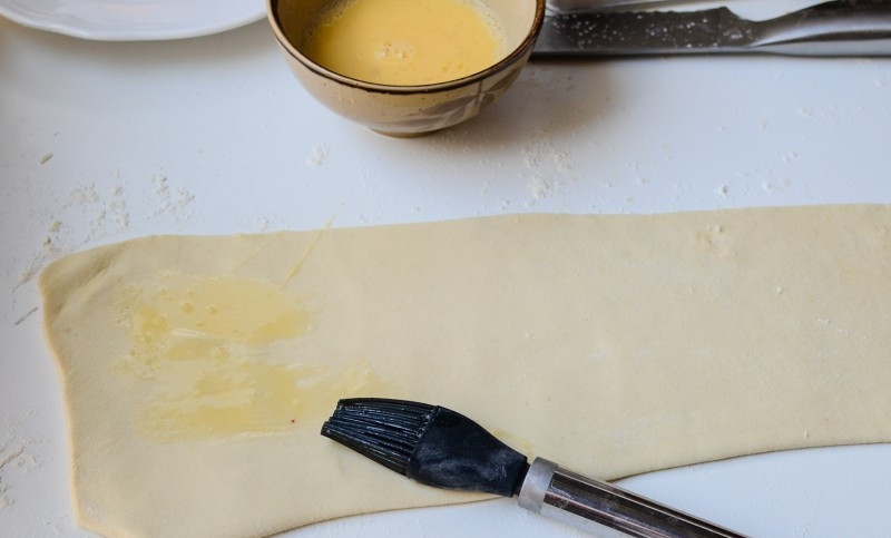 1. Этап. Слоеные палочки с сыром: Тесто раскатать в широкие полоски и смазать яйцом.