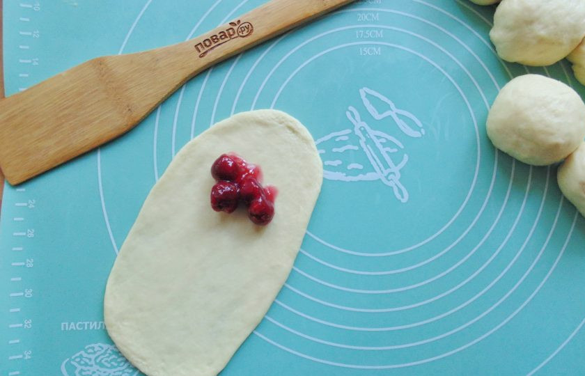 1. Этап. Дрожжевые рогалики с вишней: Раскатайте тесто в виде овала выложите начинку. У меня начинки немного с той лишь целью, чтобы она в процессе выпекания не вытекала из рогалика. Мне такого количества вишни достаточно. Вы можете класть больше.