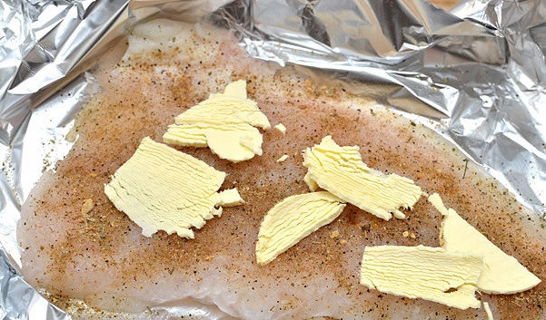 1. Этап. Минтай в духовке: 6. Сливочное масло нарежьте тонкими пластинками и распределите по филе. Лимон нарежьте кружочками и положите сверху.