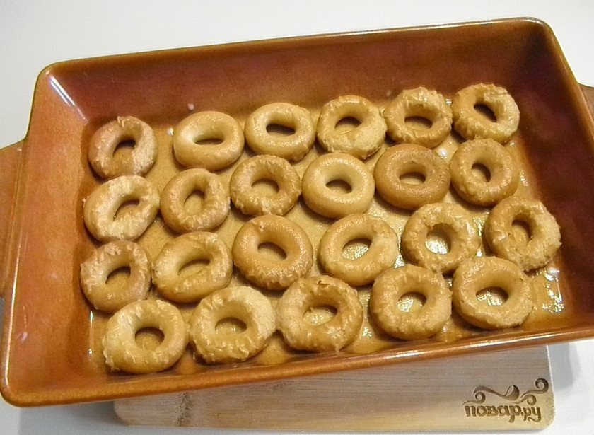 1. Этап. Бублики с фаршем в духовке: Возьмите удобный большой противень. Смажьте его растительным маслом, выложите размоченные бублики ровным слоем.