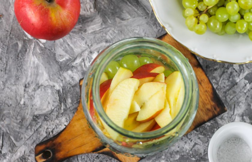 1. Этап. Компот из винограда с яблоками на зиму: Яблоки промойте, разрежьте каждое на четыре части и срежьте семенные блоки. Нарежьте каждую четвертинку ломтиками и высыпьте в емкость к винограду.