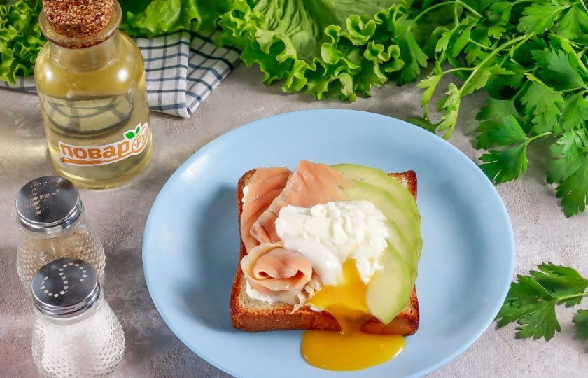 1. Этап. Тост с авокадо, соленой семгой и яйцом пашот: Разверните яйцо-пашот и удалите пищевую пленку. Выложите яйцо на тост и разрежьте.