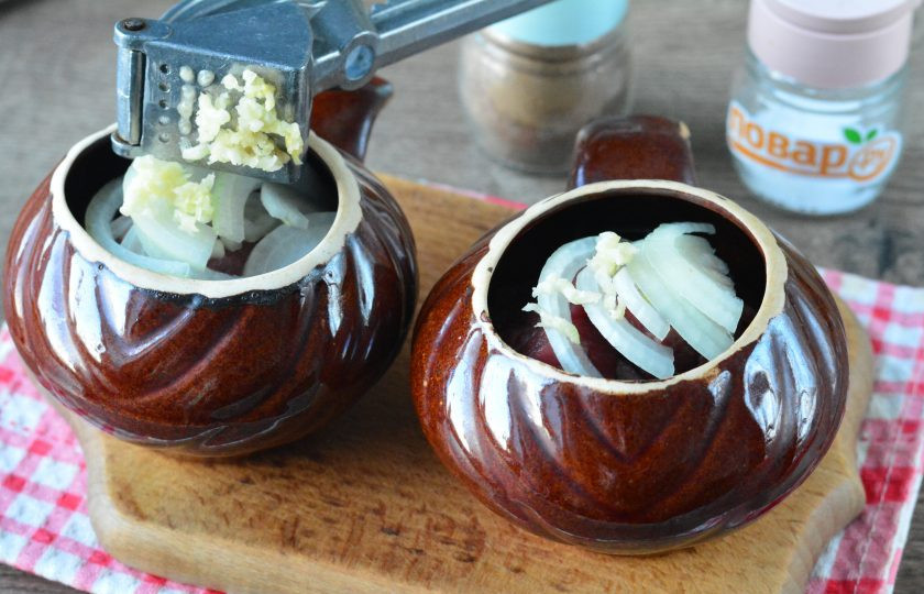 1. Этап. Томленая говядина в духовке при низкой температуре: Выложите между кусочками говядины лук, выдавите в горшочки чеснок — он придаст мясу отменный аромат.