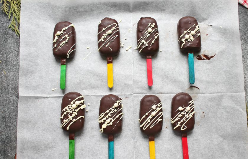 1. Этап. Пирожное Эскимо: Темный и белый шоколад измельчите и по отдельности растопите на водяной бане. Окуните каждую заготовку эскимо в темный шоколад, дайте стечь лишнему шоколаду и выложите на пергамент. Дайте застыть шоколаду и сделайте рисунок на поверхности из белого шоколада. При желании украсьте еще и дополнительным декором. Уберите пирожные в холодильник, чтобы шоколад застыл.