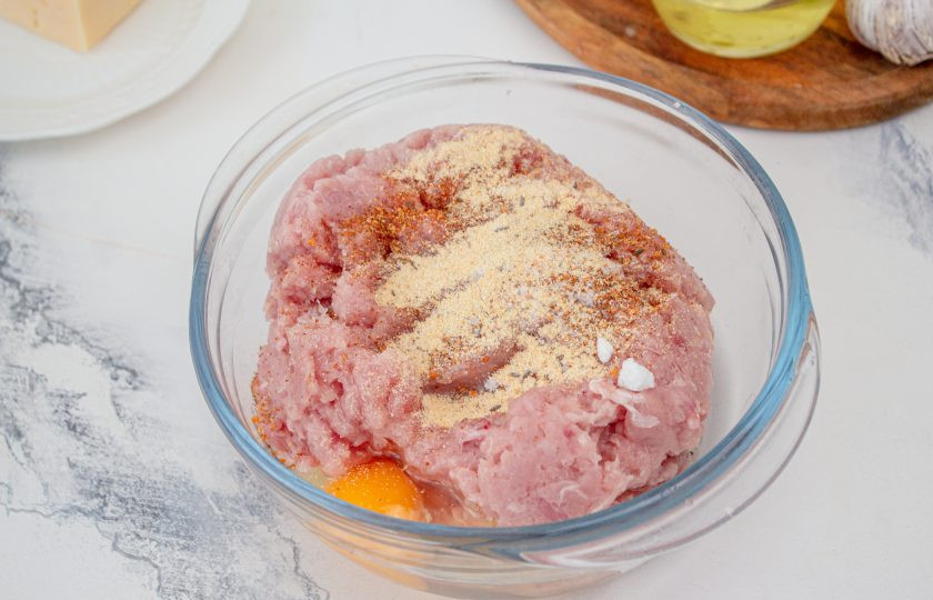 1. Этап. Куриные котлеты с сыром в мультиварке: К фаршу вбейте яйцо, добавьте специи для курицы, соль и перец. Тщательно перемешайте.