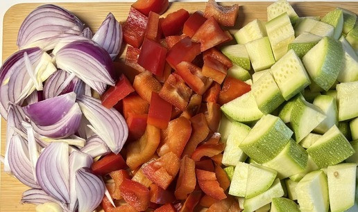 1. Этап. Паста с овощами и фетой из духовки: Помыть овощи под проточной водой, почистить. Нарезать цуккини и болгарский перец кубиками, красный лук нарезать на 8 частей вдоль, чеснок шайбами.