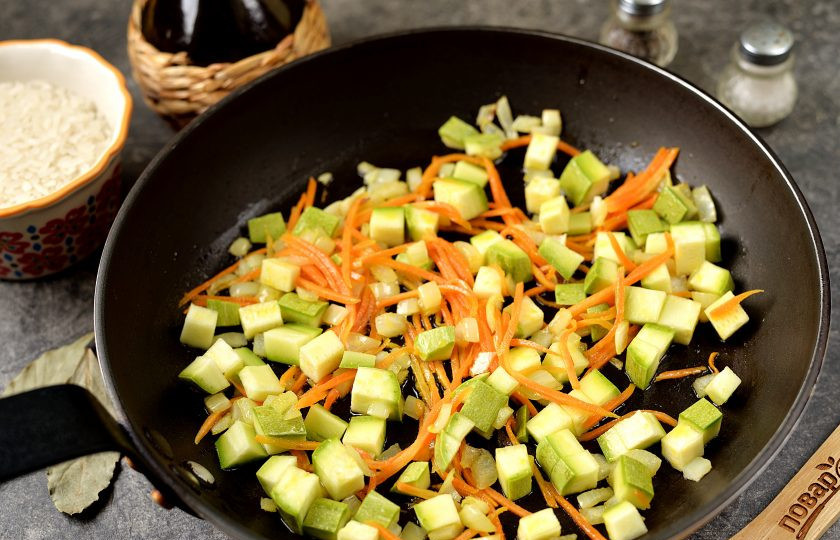 1. Этап. Рис с колбасками и овощами: Нарежьте мелко репчатый лук и кабачок, нашинкуйте морковь. Разогрейте в сковороде растительное масло, обжарьте на нем овощи минуты 2-3 на умеренном огне.