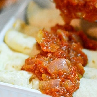 1. Этап. Энчиладас: 7. Заверните тортильи с сыром в прямоугольные конвертики, выложите в форму для запекания. Сверху полейте соусом и посыпьте немного сыра.