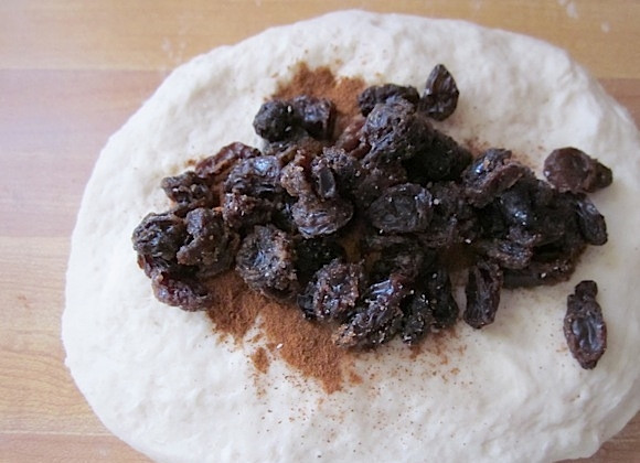 1. Этап. Вкусные бублики: 5. Разделите тесто на 2 части. Одну отложите, а вторую разомните руками в небольшую лепешку, посыпьте его корицей и добавьте изюм.