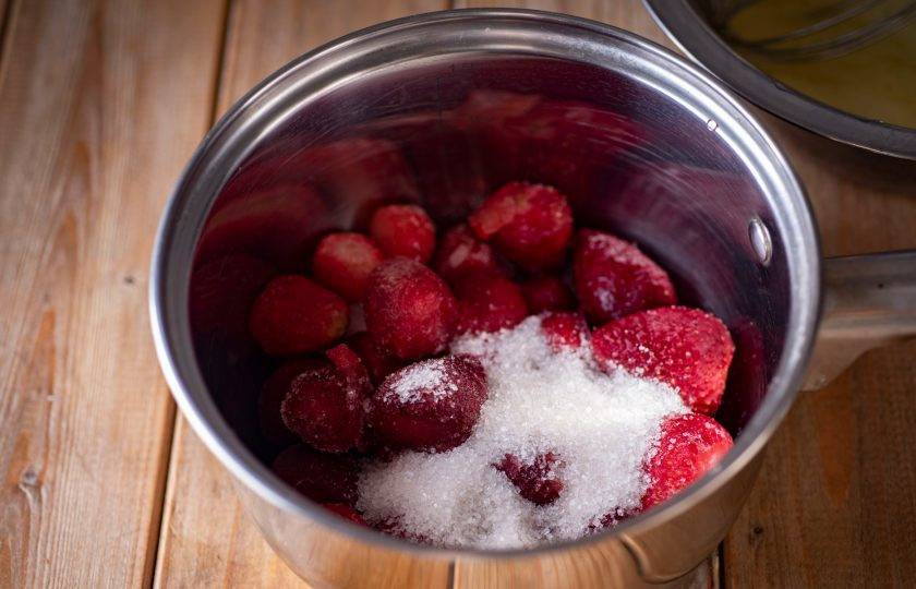 1. Этап. Молочное мороженое с клубникой: В сотейник выложите замороженную клубнику и добавьте к ней 40 грамм сахара. Поставьте на небольшой огонь и дождитесь закипания сиропа — весь сахар должен раствориться.