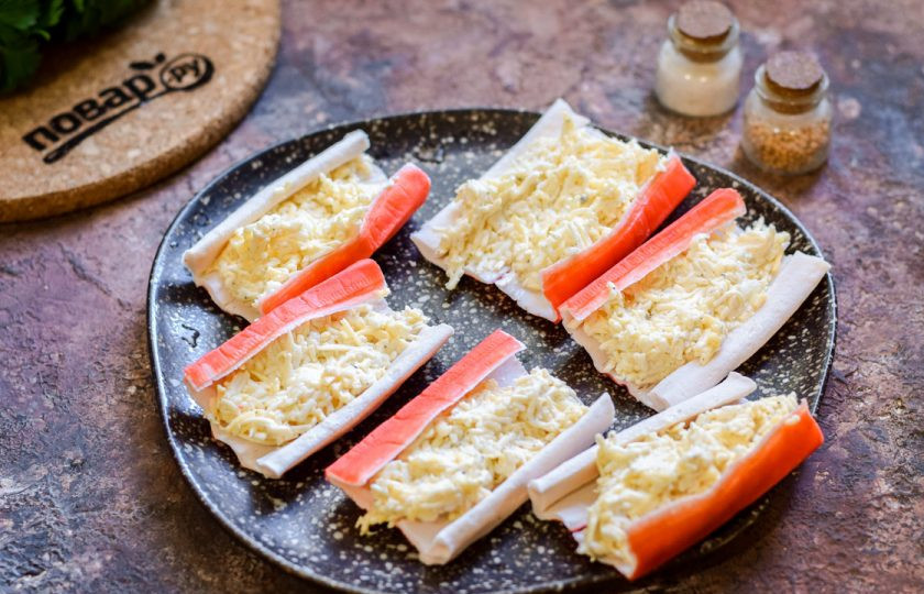 1. Этап. Крабовые палочки Очаровашки: Крабовые палочки разверните, переложите на каждую палочку по ложке сырной начинки.