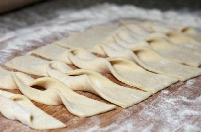 1. Этап. Печенье Хворост: Охлаждённое тесто нужно раскатать слоем около четырёх миллиметров. Затем получившийся пласт надо нарезать на полоски шириной около пяти сантиметров. В каждой полоске нужно сделать надрез посередине. Выверните тесто через этот надрез.