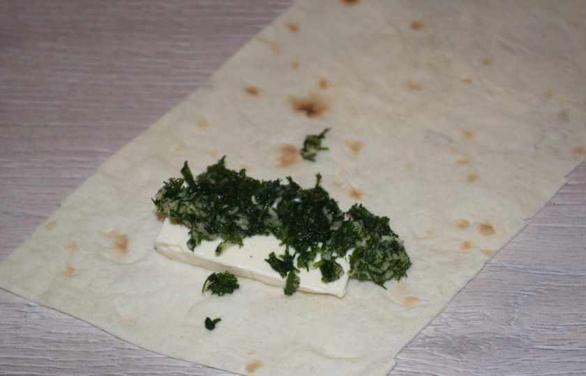 1. Этап. Палочки из лаваша с начинкой: На полоску лаваша выложите чайную ложку измельченной зелени и один брусочек сырка. Сверните лаваш в рулетик.