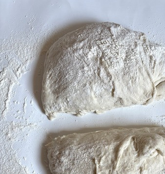1. Этап. Быстрые багеты: Включить духовку для разогрева на 240 градусов. Присыпать стол мукой, аккуратно выложить тесто, поделить на две части, присыпая мукой.