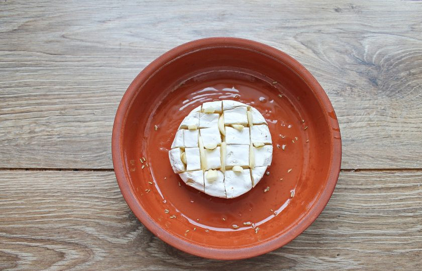 1. Этап. Камамбер с багетом в духовке: Камамбер разрежьте не доходя ножом до дна на квадратики. Вставьте в разрезы оставшийся чеснок порезанный на кусочки. Форму для запекания смажьте маслом со специями и выложите в середину сыр.