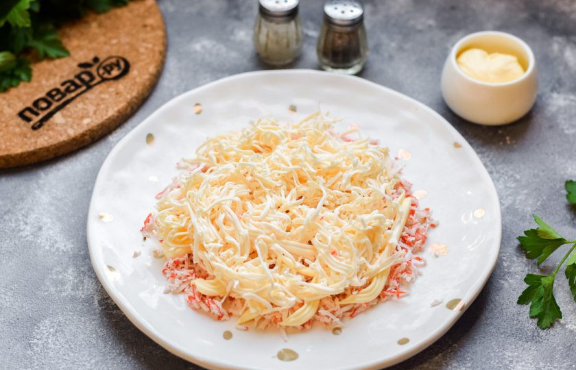 1. Этап. Тертый крабовый салат: Поверх крабовых палочек натрите плавленый сыр. Это будет второй слой салата.