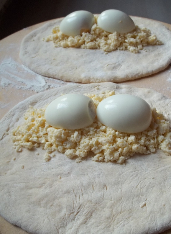 1. Этап. Хачапури по-гурийски: Затем разделите тесто на несколько шариков, желательно больших, так как хачапури традиционно делают большими. Раскатайте их и на одну сторону выложите 2-3 столовых ложки творожного сыра и сверху уложите две половинки варёного яйца.