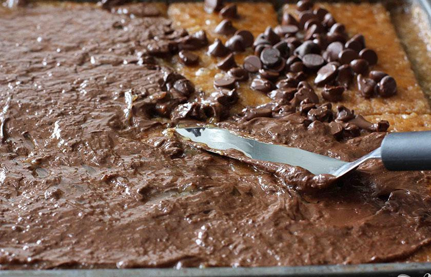 1. Этап. Шоколадные пирожные с миндалем: 4. Достать противень из духовки, посыпать сверху шоколадными чипсами, снова поставить в духовку и дать шоколаду расплавится в течение приблизительно 1 минуты. Затем ложкой или шпателем равномерно распределить его по карамельной смеси на крекерах.