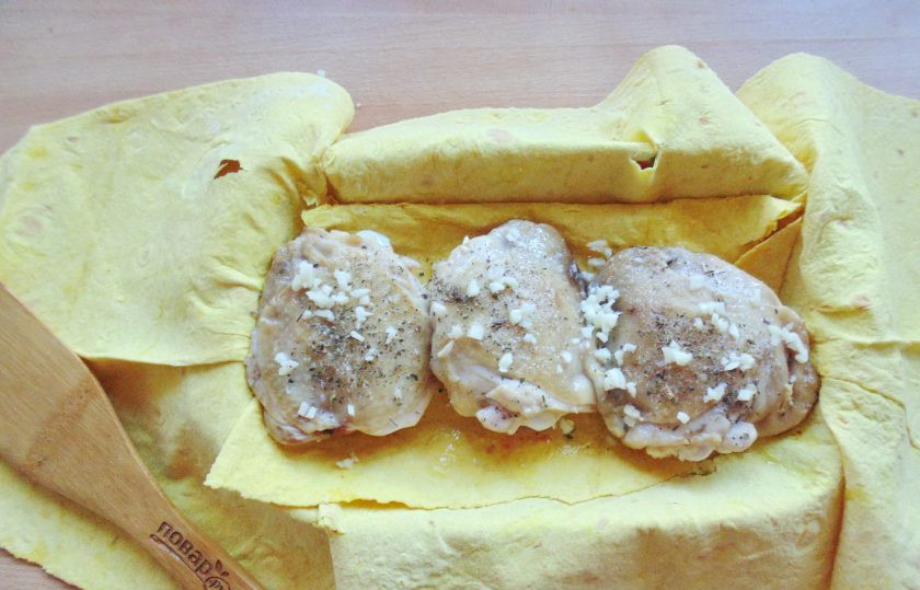 1. Этап. Бедрышки в лаваше в духовке: В форму для запекания выложите лист лаваша. На листе разложите куриные бедрышки. Посолите, поперчите и посыпьте сухим базиликом. Чеснок измельчите и посыпьте куриное мясо.