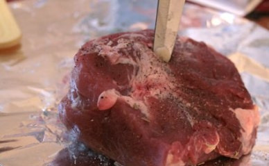 1. Этап. Свинина с розмарином в духовке: Очищаем зубчики чеснока и нарезаем тонкими пластинками. Острым ножом делаем в мясе проколы и вставляем в них чеснок.