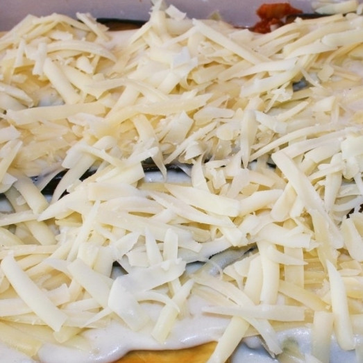 1. Этап. Мусака по-гречески: 5. В большую форму для запекания влейте половину количества соуса с фаршем. Сверху выложите слой баклажанов (половину количества, затем снова мясной соус и оставшиеся баклажаны. Залейте все соусом Бешамель. Сверху посыпьте тертым сыром.