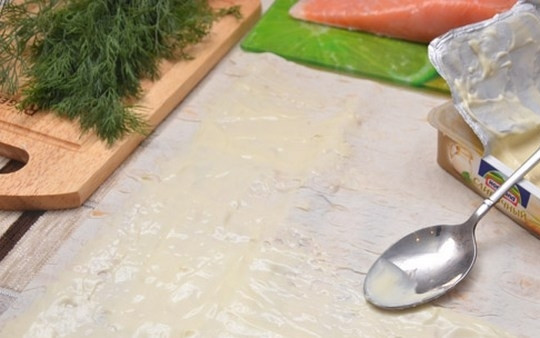 1. Этап. Лаваш с сыром, и семгой, и зеленью: 1. Достаю лаваш из упаковки, раскрываю его на столе. Плавленый сыр у меня в пастообразной форме, поэтому с помощью ложки намазываю его на всю поверхность лаваша (оставляю по 1 сантиметру с каждого края).