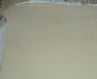 1. Этап. Слоеный сырный пирог: Готовое слоеное тесто делим на две части. У нас будет два пирога. Раскатываем часть теста на присыпанной мукой поверхности в пласт толщиной примерно 0,5 см.