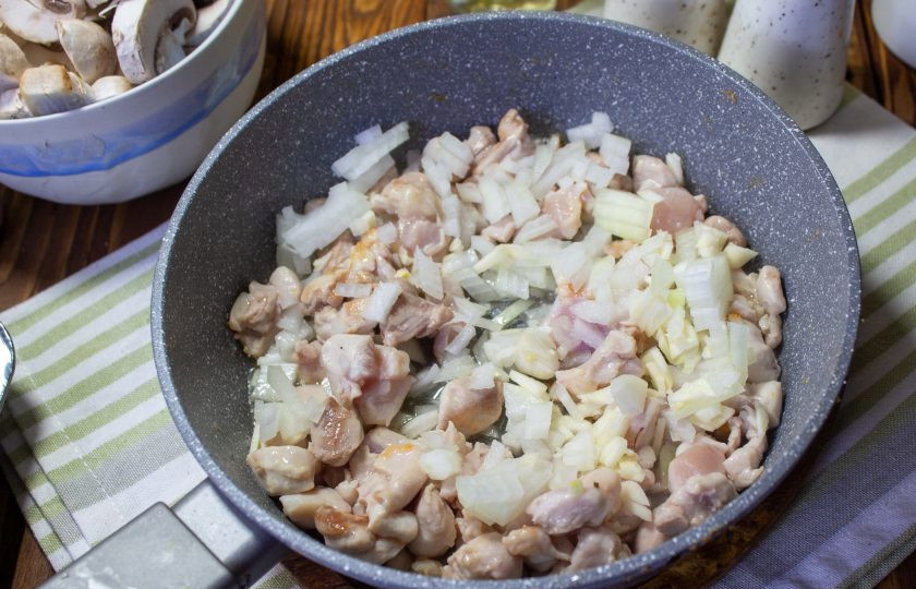 1. Этап. Жульен с курицей и грибами в формочках для кекса: Добавьте в сковороду масло. Лук и чеснок мелко нарежьте и тоже добавьте к курице, обжаривайте несколько минут, до мягкости овощей.