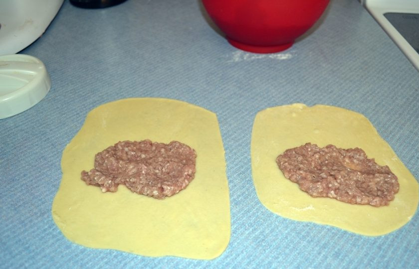 1. Этап. Чебуреки домашние с мясом: 7. На каждую заготовку из теста выложите по 2 чайные ложки мясной начинки, заверните тесто на начинку и немного прижмите.
