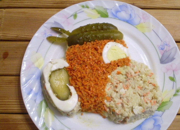 1. Этап. Салат Обезьянка с корейской морковкой: С помощью белка сделайте уши, вложите огурчик, сделайте косынку пирату. Морду начните выкладывать мелко порезанной морковью.