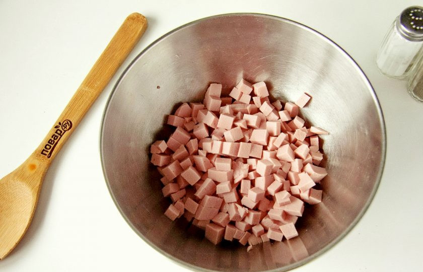 1. Этап. Оливье без моркови: Колбасу нарежьте небольшими кубиками и сложите в глубокую миску или салатник.