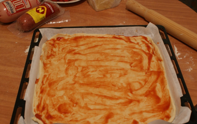 1. Этап. Пицца из дрожжевого теста: 1. Готовое дрожжевое тесто размораживаем при комнатной температуре и раскатываем толщиной не более 1 сантиметра по размеру формы для выпекания. На противень укладываем пергамент, затем кладем тесто и смазываем его кетчупом (тут можно брать сколько любите).